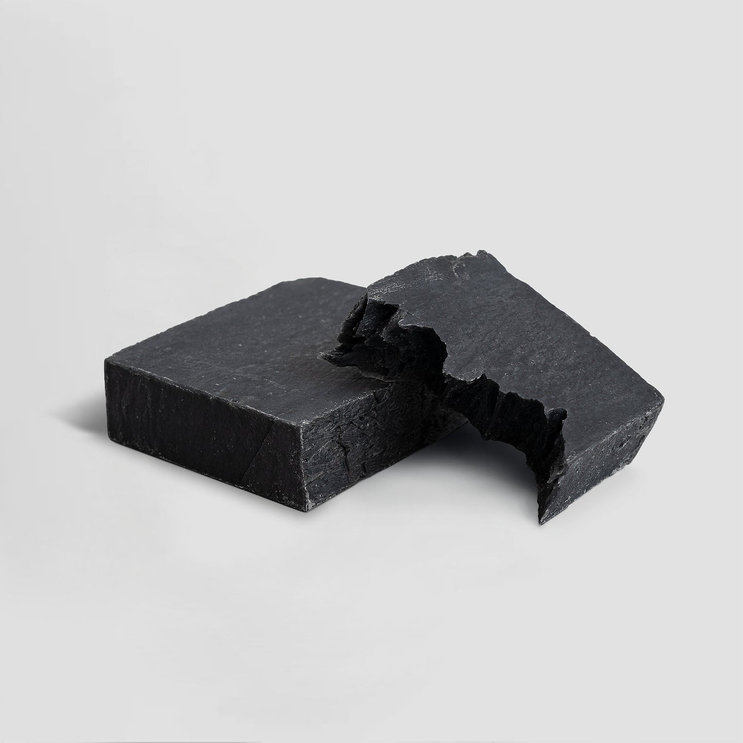 Two pieces of black soap on a light gray background