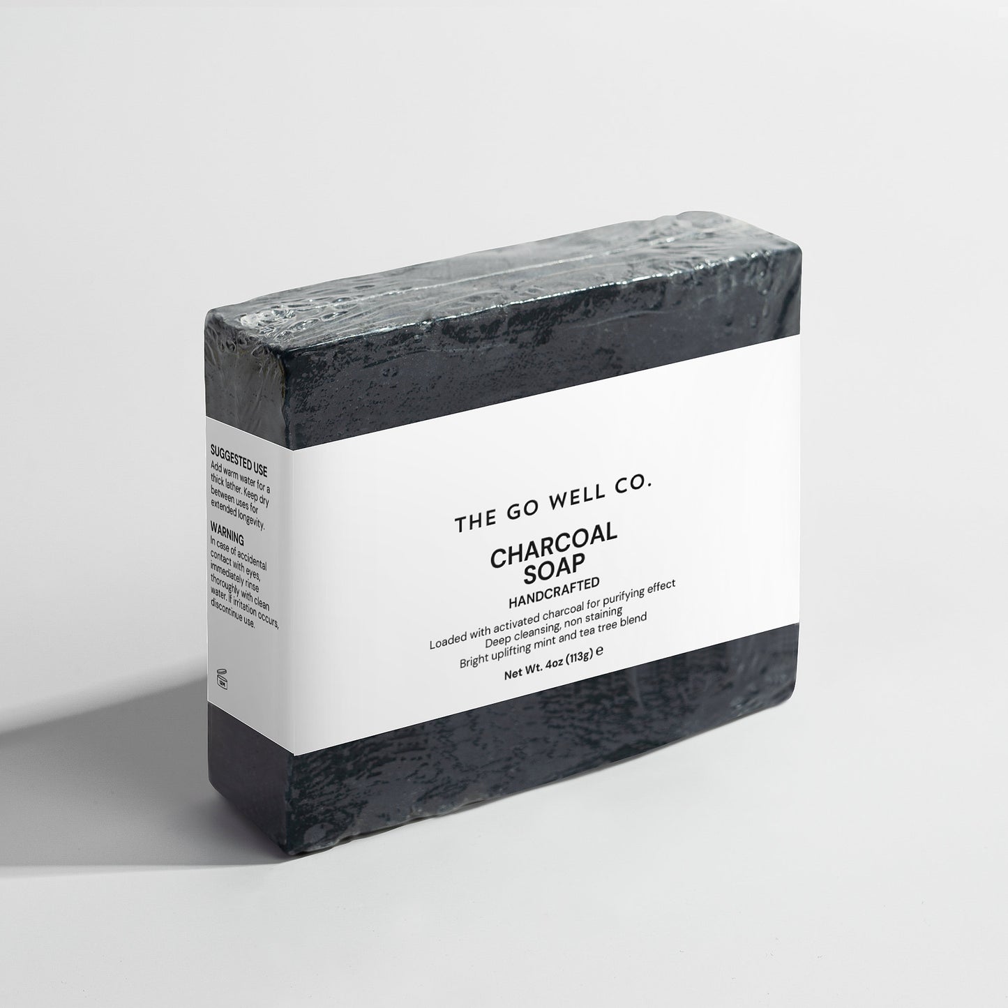 Bar of charcoal soap with a white label on a light gray background