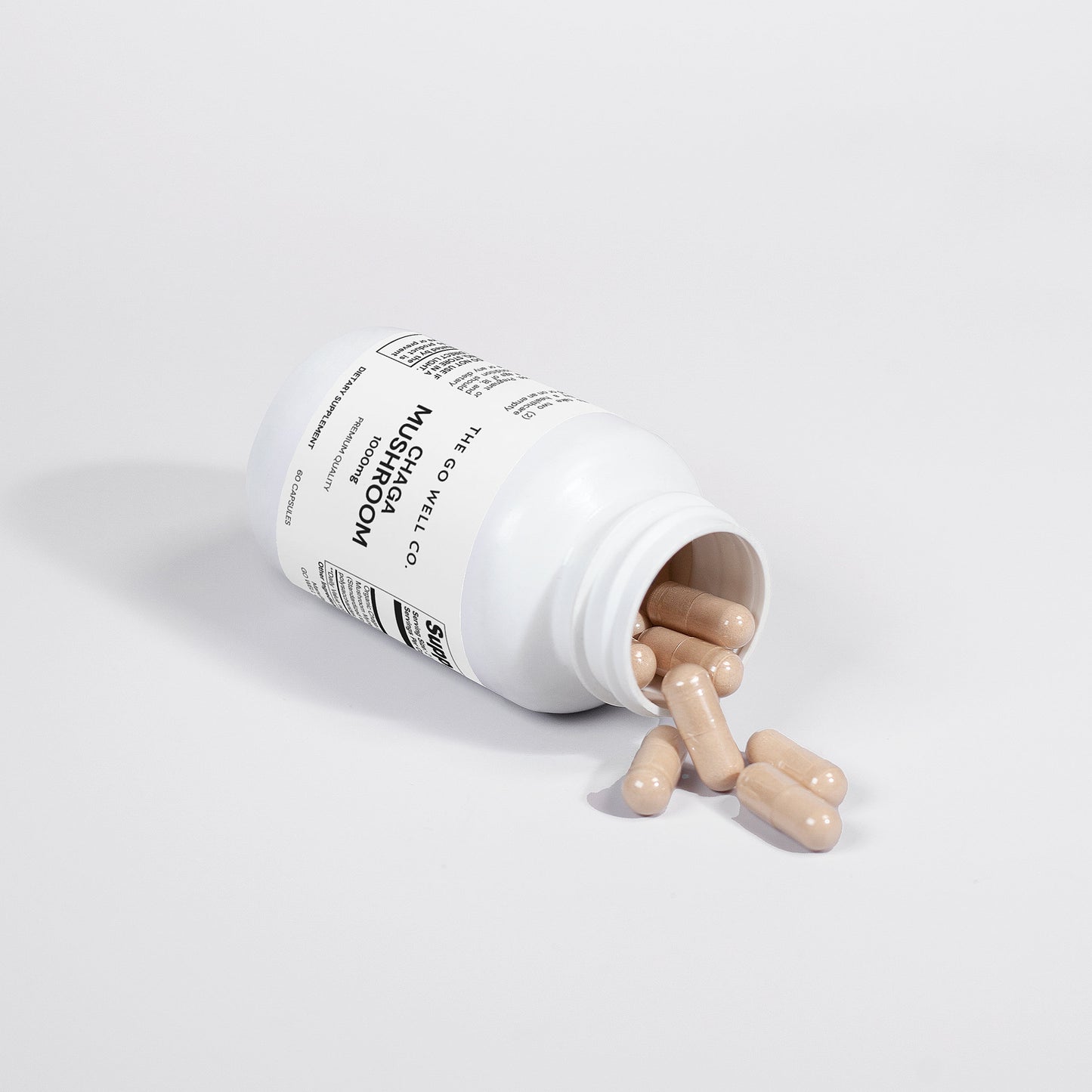 White supplement bottle with mushroom capsules spilling out on a light gray background