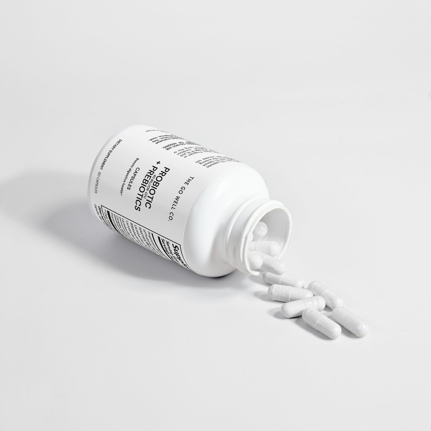 White probiotic supplement bottle with pills spilling out on a light gray background