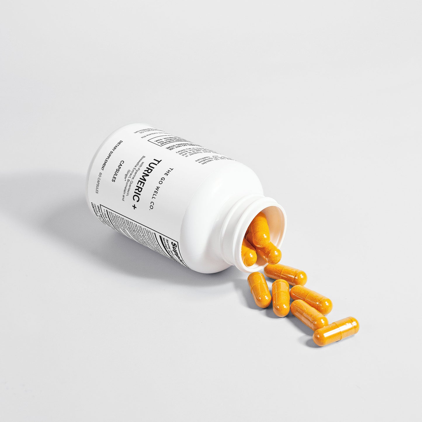 Open white supplement bottle with yellow capsules spilling out on a light gray background