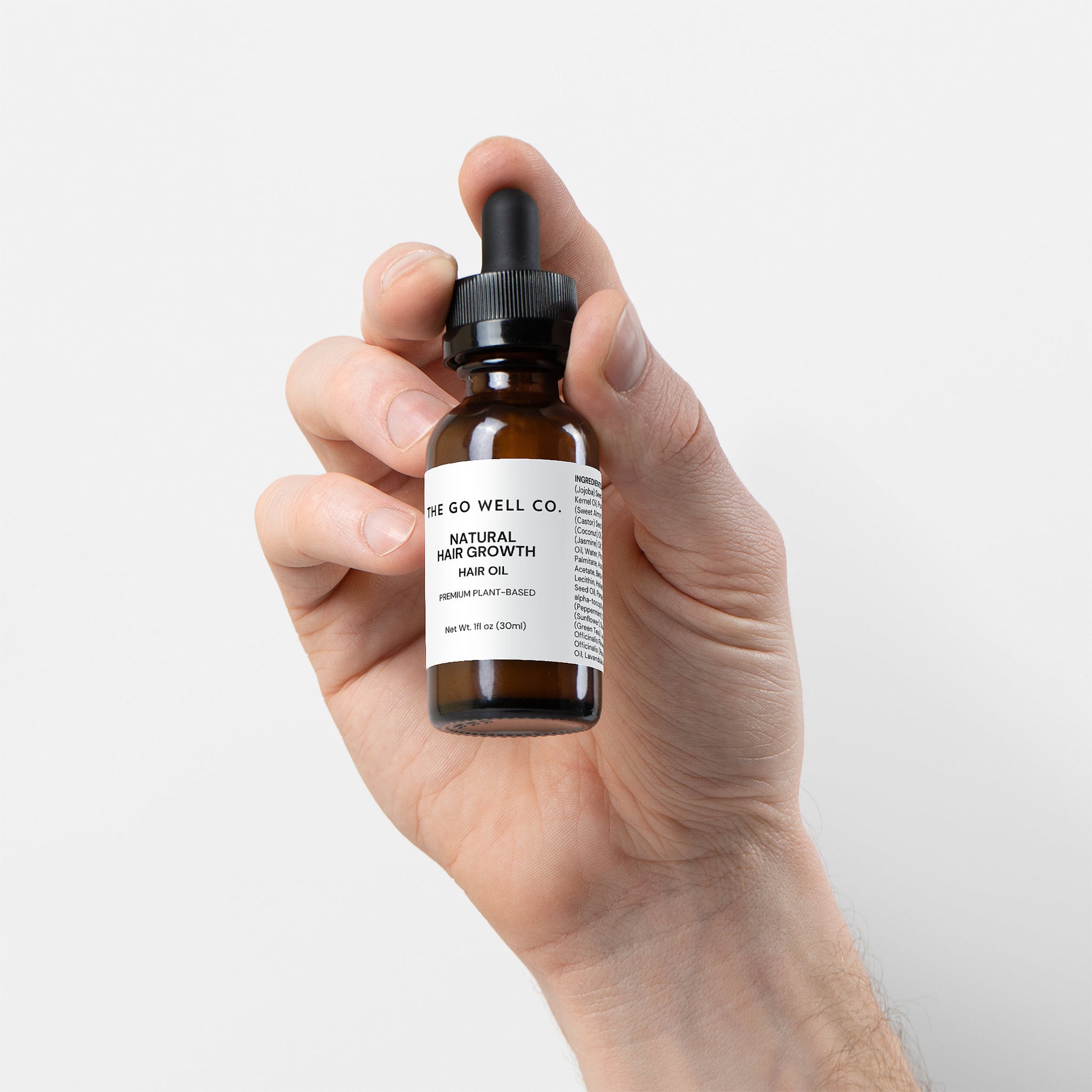 Hand holding a bottle of 'The Go Well Co.' natural hair growth oil against a light background