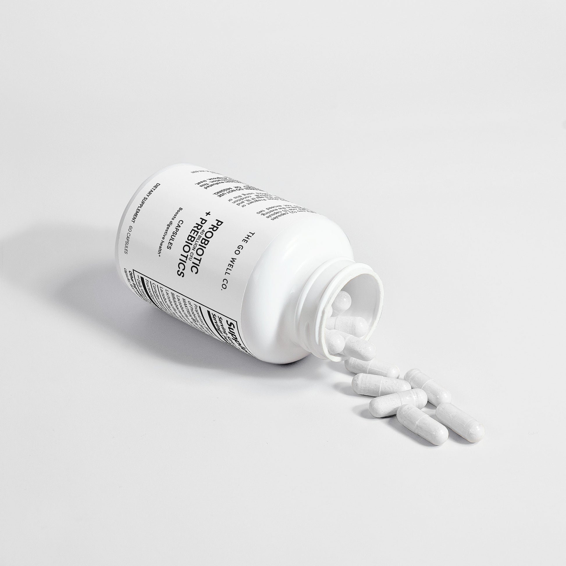 White probiotic supplement bottle with pills spilling out on a light gray background