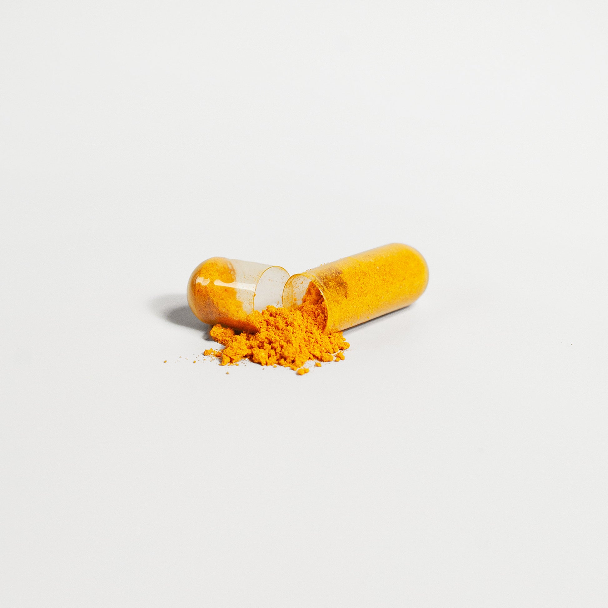 Open capsule with yellow powder on a white background